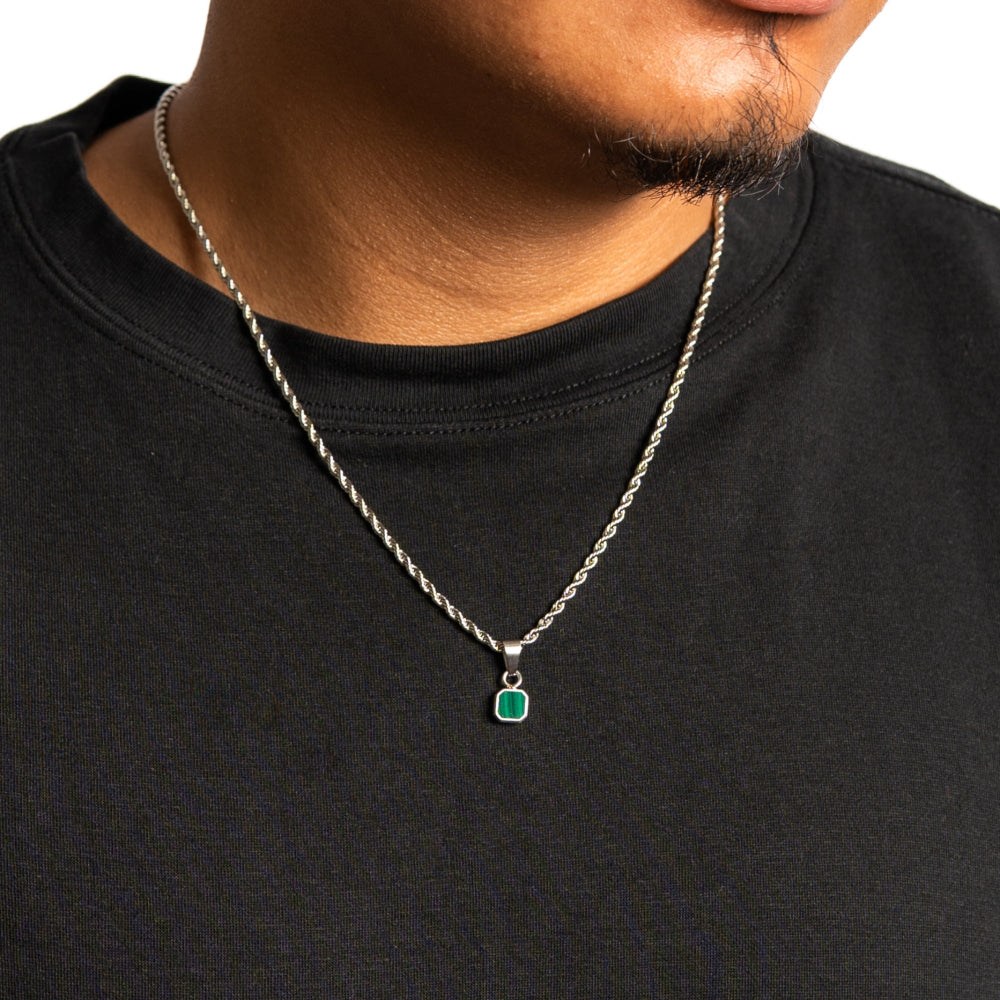Person wearing a black shirt with a silver necklace featuring a green pendant.