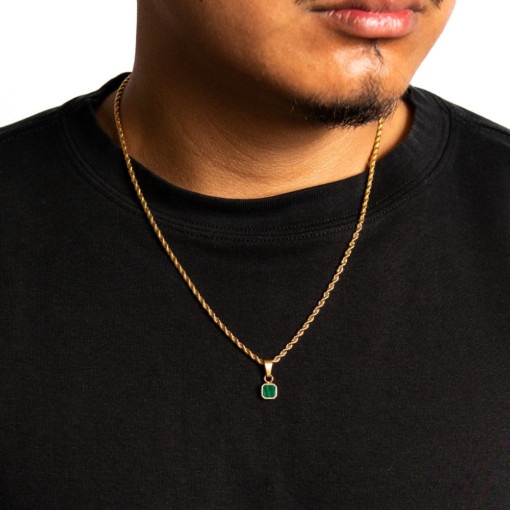 Man wearing a gold chain necklace with a green pendant on a black shirt.