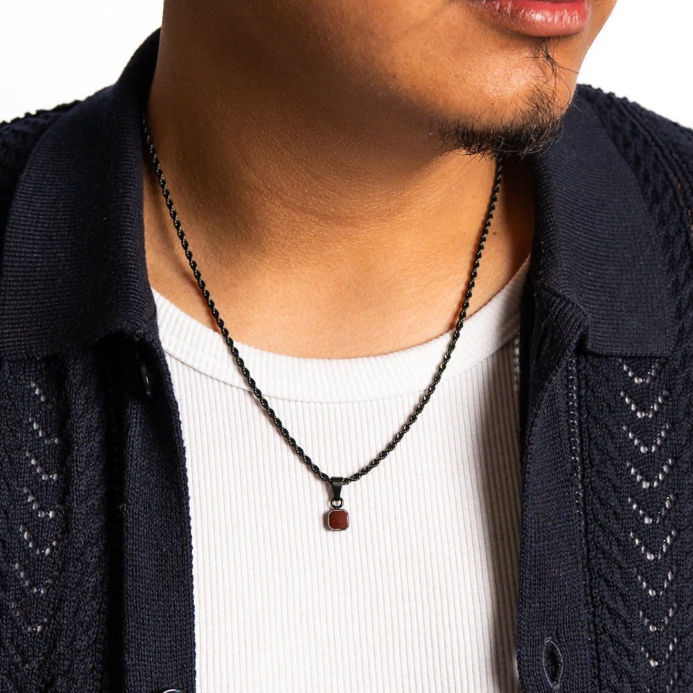 Person wearing a dark blue cardigan over a white shirt with a necklace featuring a red stone.