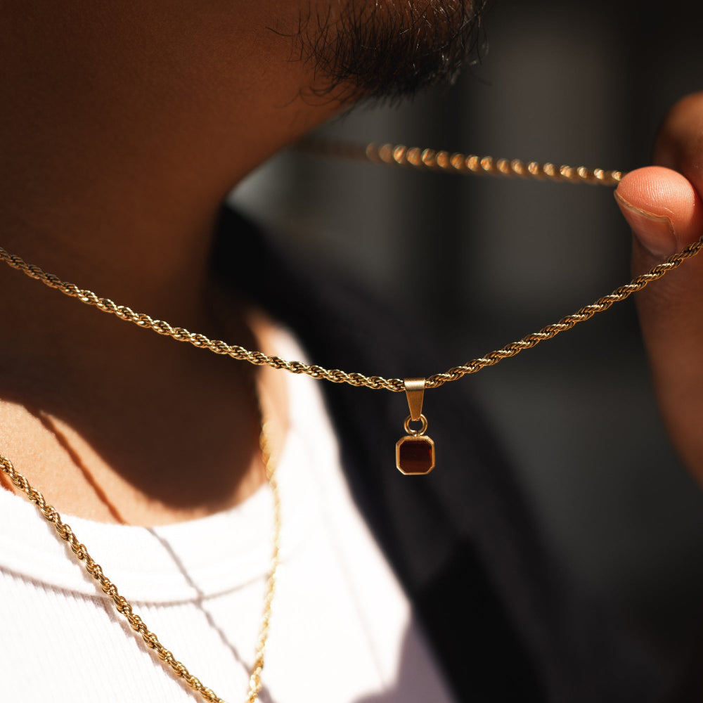 Close-up of a person wearing two gold necklaces with pendants against a dark background