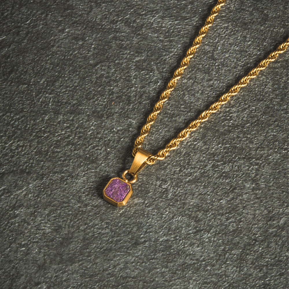 Gold necklace with a purple pendant on a dark gray surface