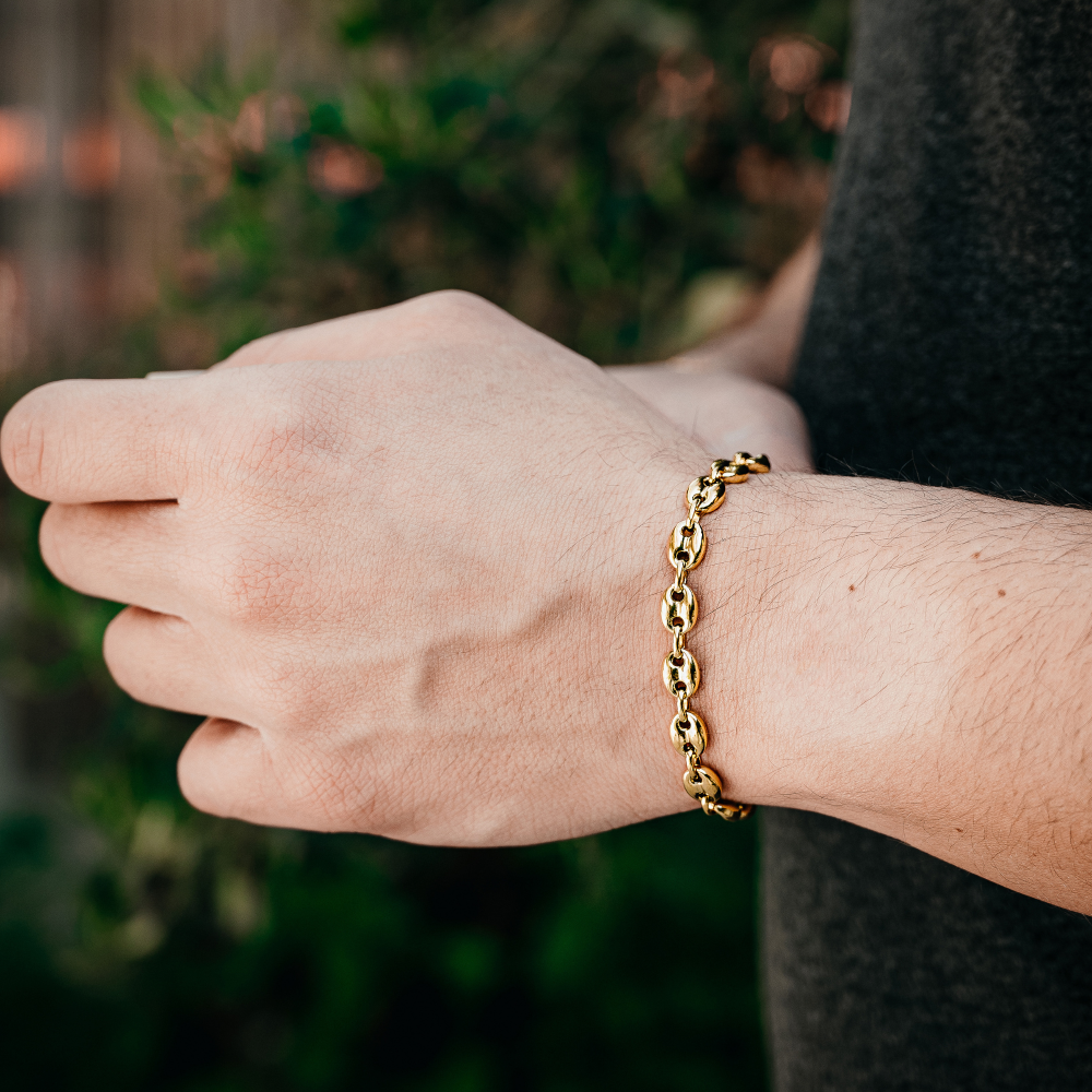 Gold chain bracelet on a wrist with a blurred green background