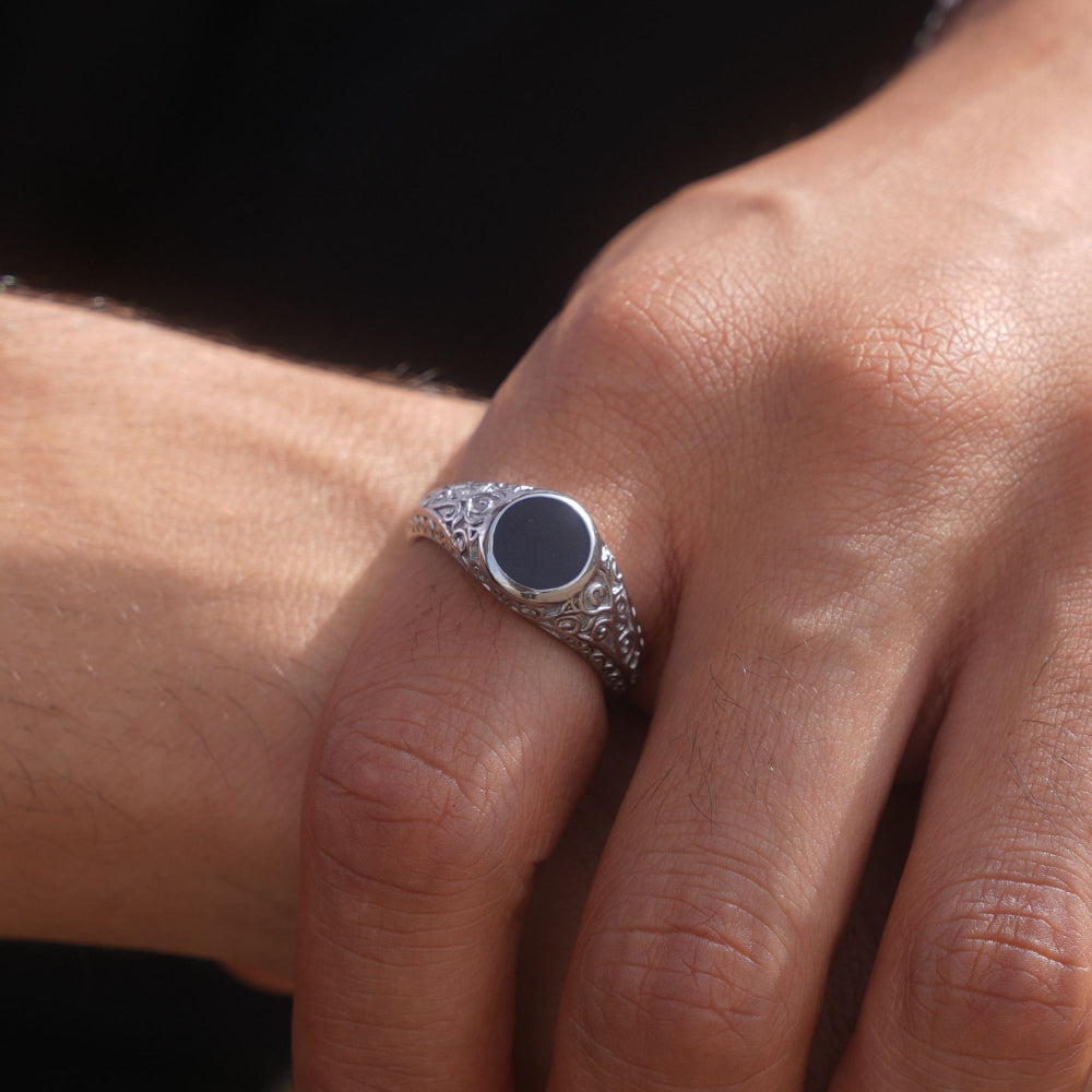 Silver ring with a dark stone on a person's finger against a black background