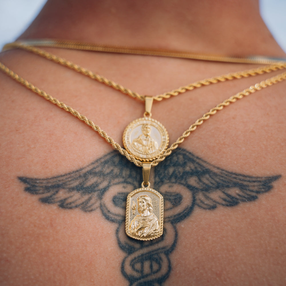 Two gold necklaces with pendants on a person's neck against a blurred background