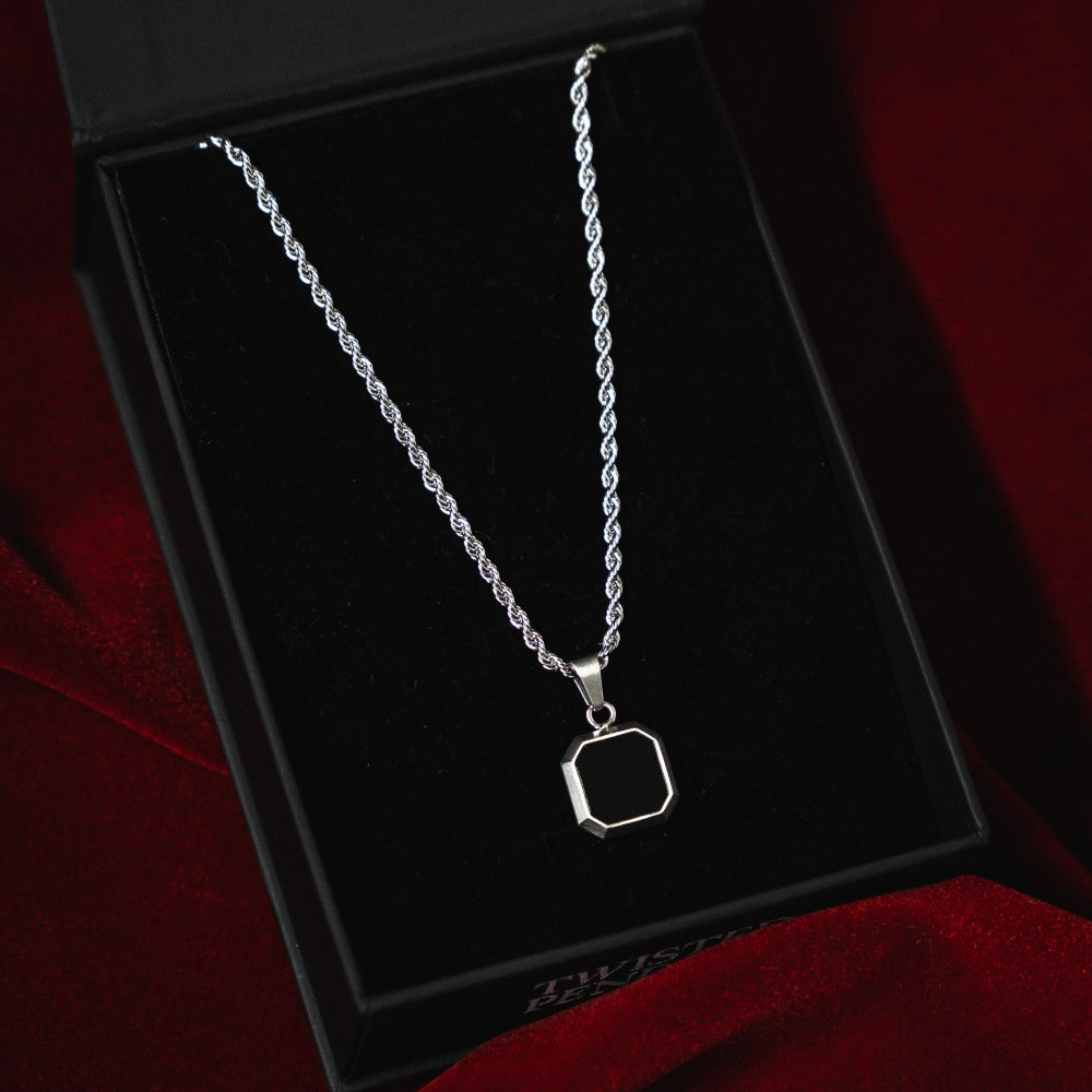 Silver necklace with a hexagonal pendant on a black box with red fabric background