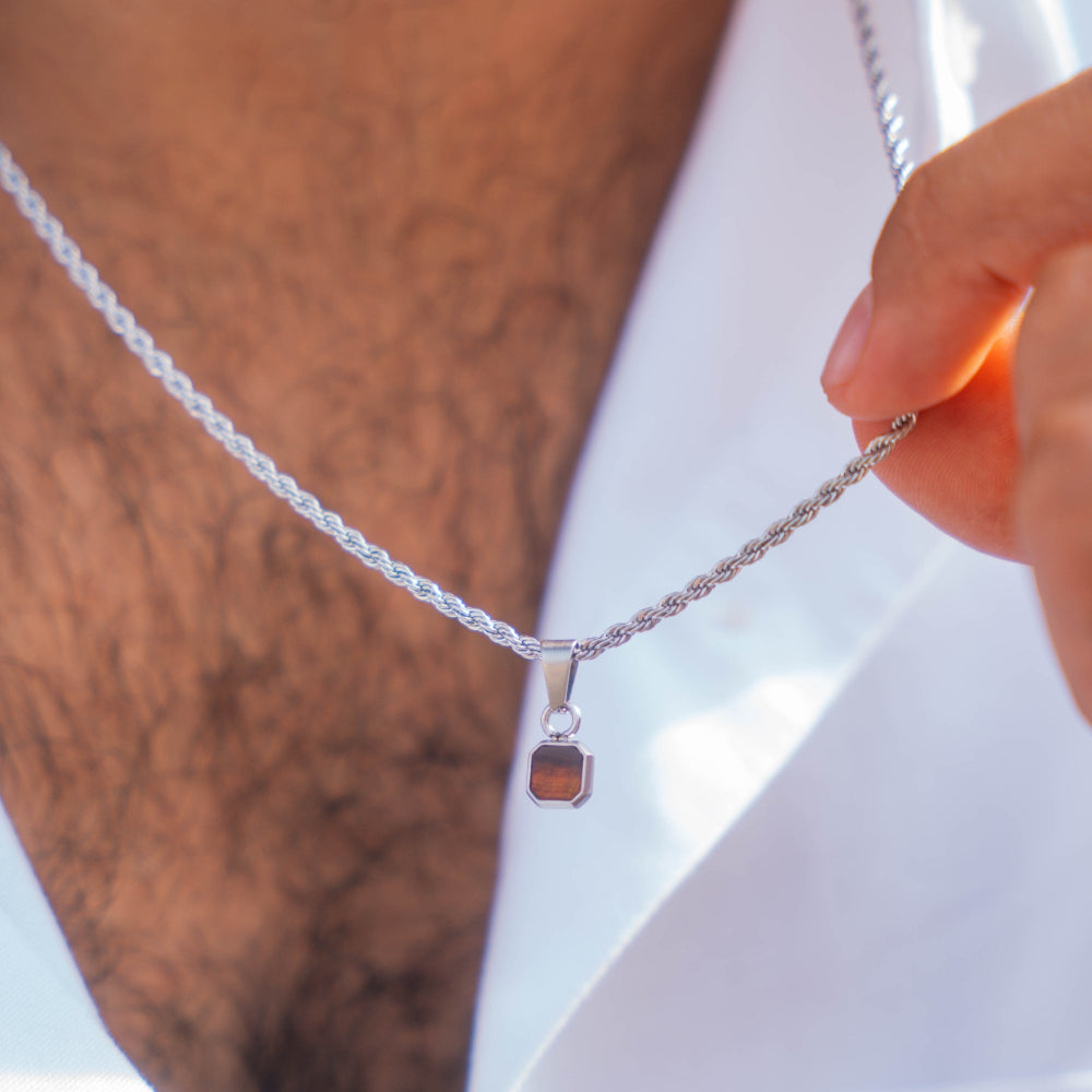 Silver necklace with a pendant held by a hand against a neutral background