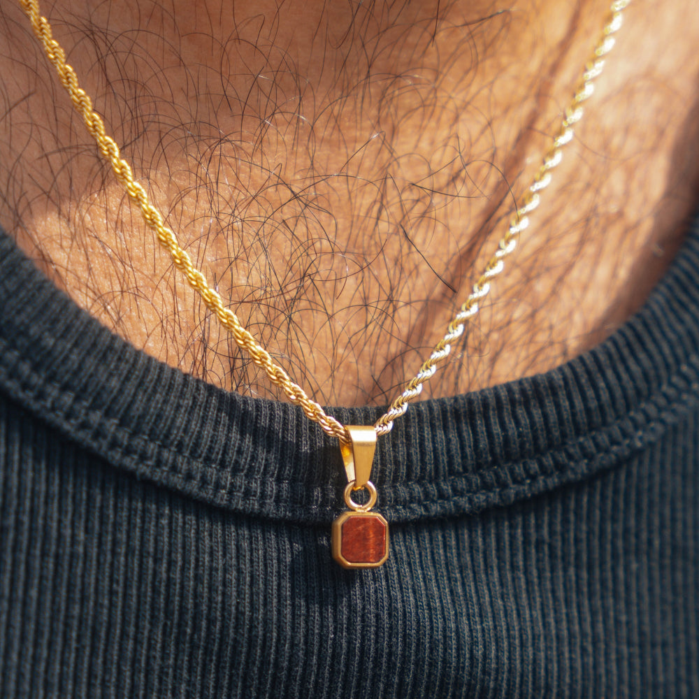 Gold necklace with a pendant on a person wearing a black shirt.