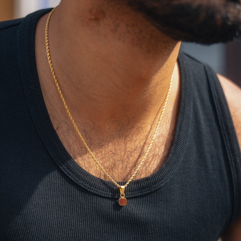 Person wearing a gold necklace with a small pendant on a blurred background