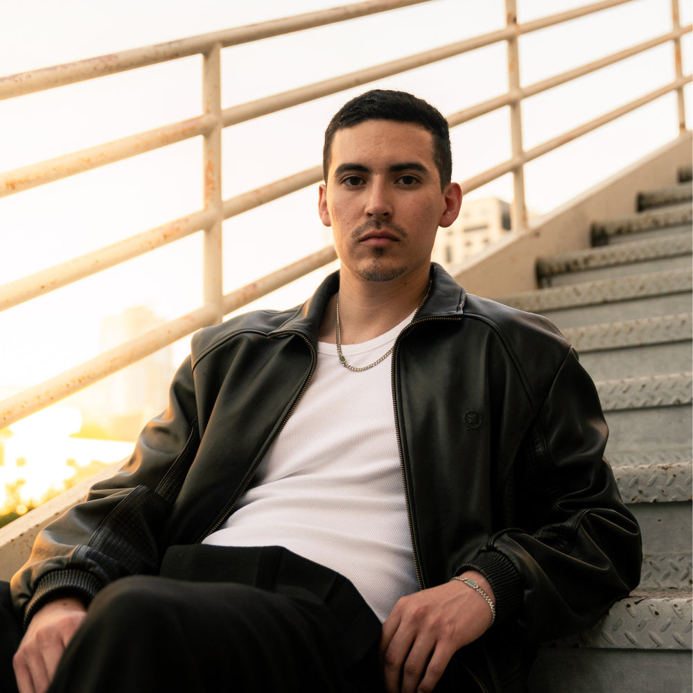 Man sitting on steps wearing a black leather jacket and white shirt.