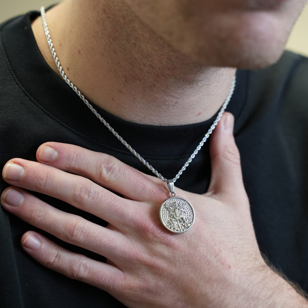 Person wearing a silver necklace with a pendant, hand resting on chest.