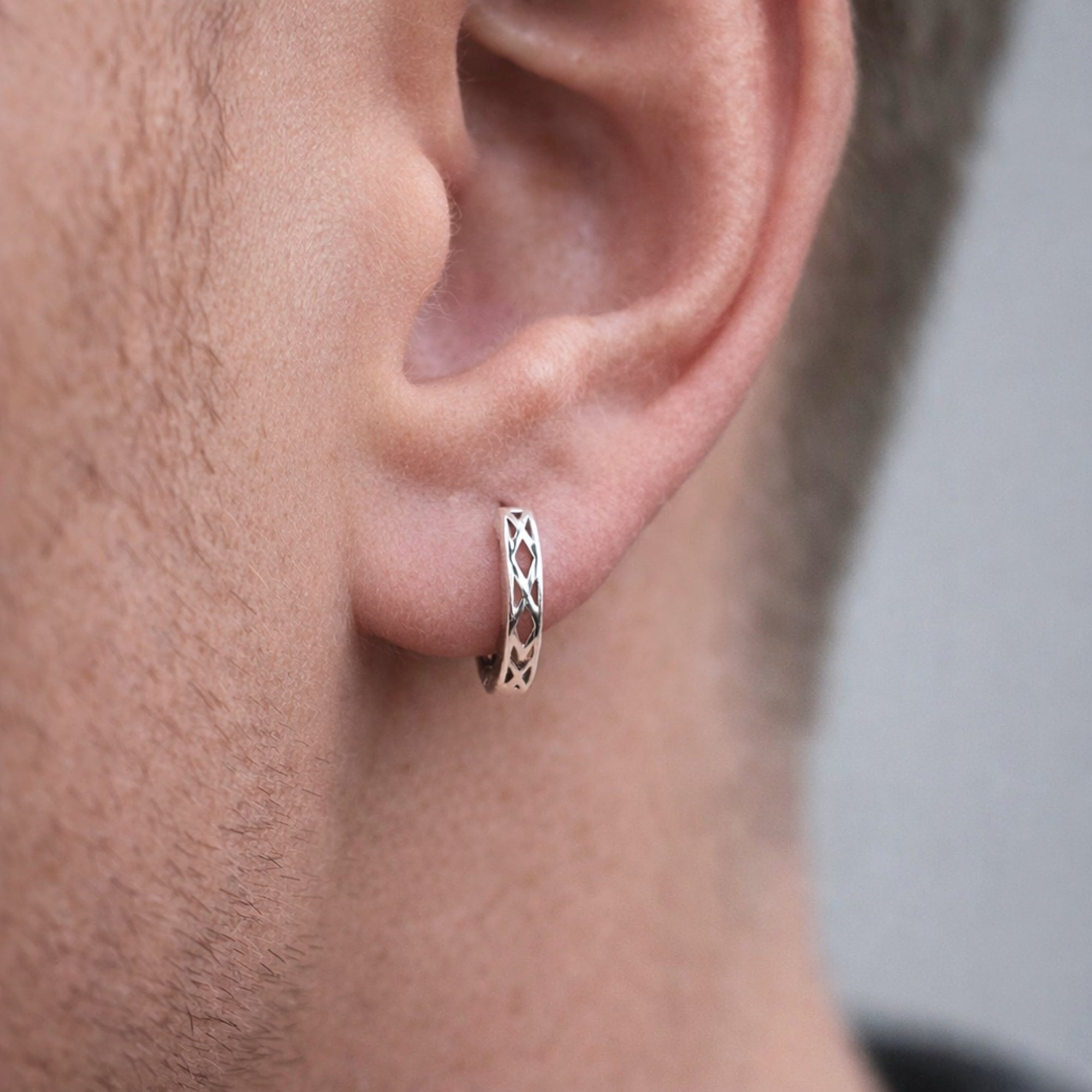 Close-up of an ear wearing a small hoop earring with a patterned design.