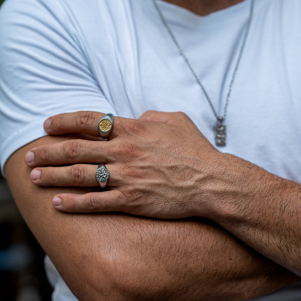 Close-up of a person's arm with two rings on the fingers, wearing a white shirt.