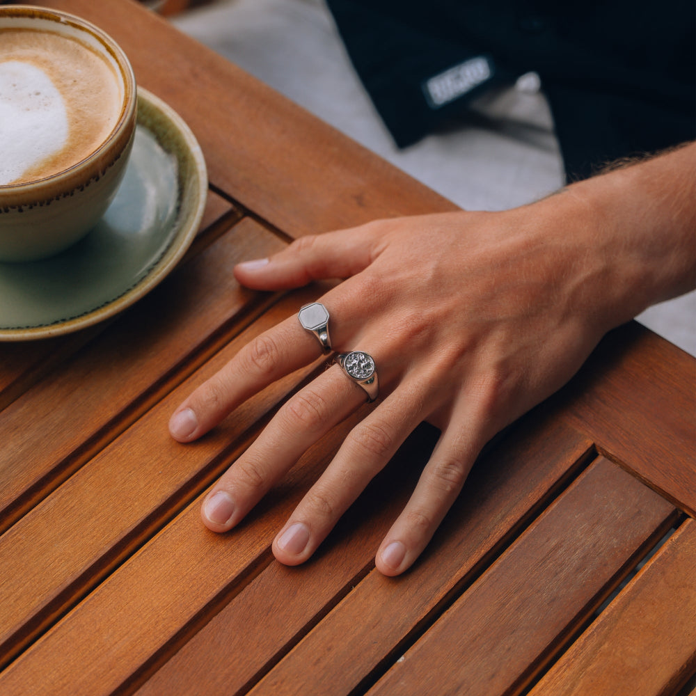 Hand with rings on a wooden table next to a cup of coffee