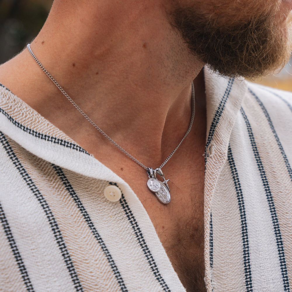 Close-up of a person wearing a necklace with a pendant, set against a blurred background.