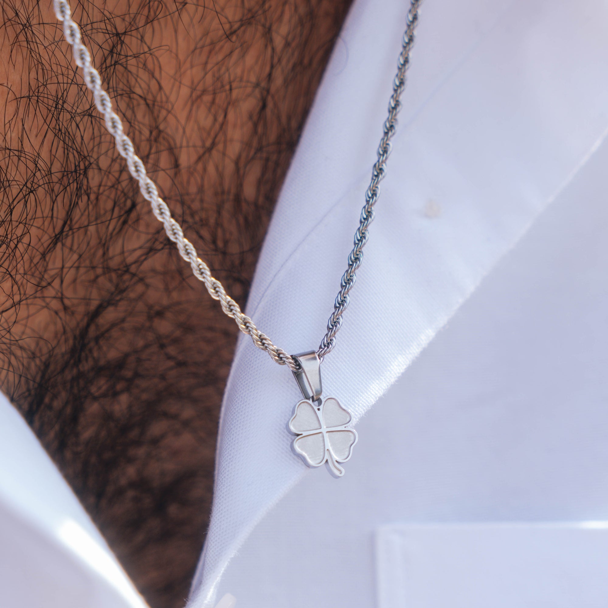 Silver necklace with a clover pendant on a white surface.