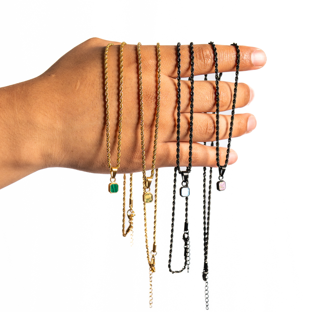 Hand wearing multiple gold and black necklaces on a white background