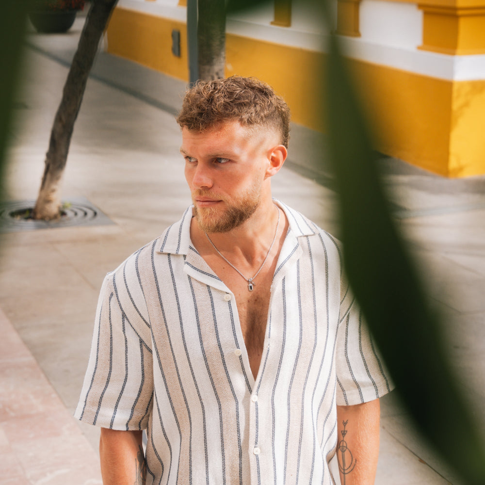 Man wearing a striped shirt standing outdoors with a blurred background