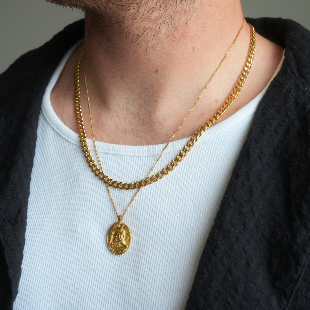 Person wearing a gold chain necklace with a pendant on a plain background