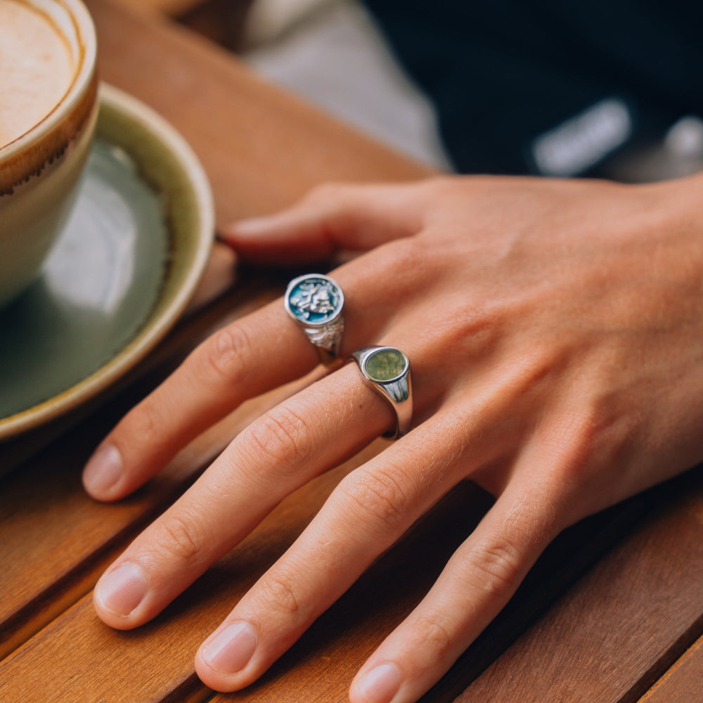 Hand with two rings on a wooden table next to a cup of coffee
