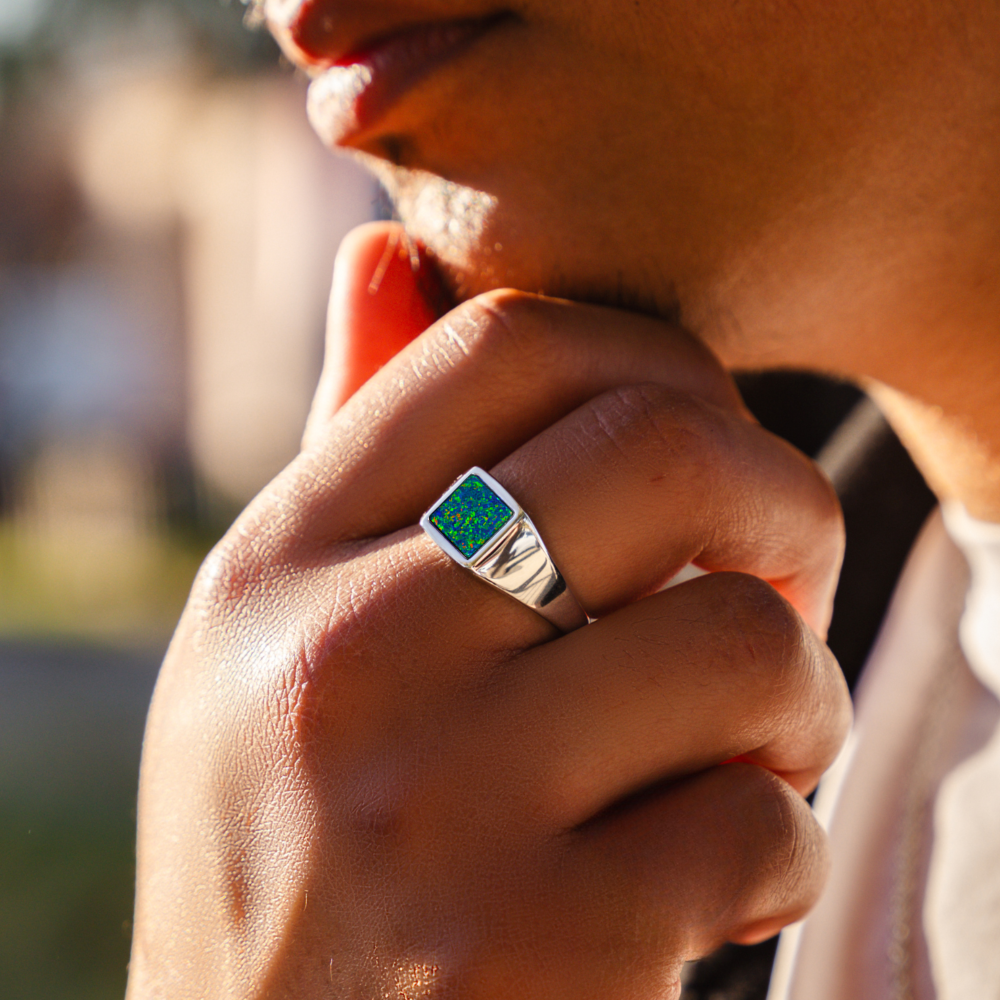 Close-up of a hand wearing a ring with a green gemstone, blurred background