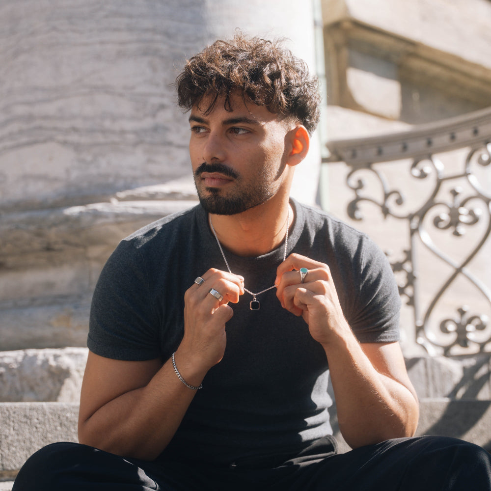 Man sitting outdoors wearing a black t-shirt and holding a necklace.