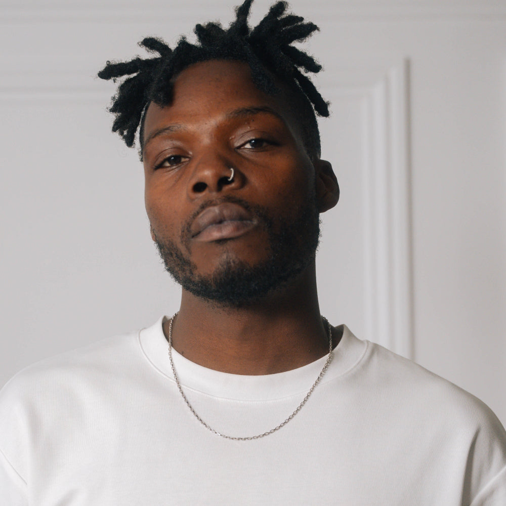 Man wearing a white shirt and gold chain against a plain background