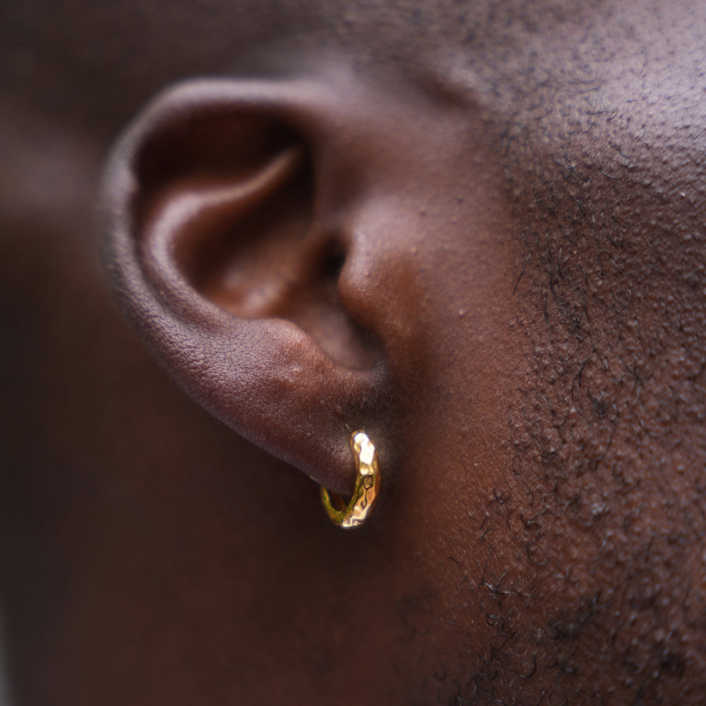 Close-up of an ear wearing a gold hoop earring with a blurred background