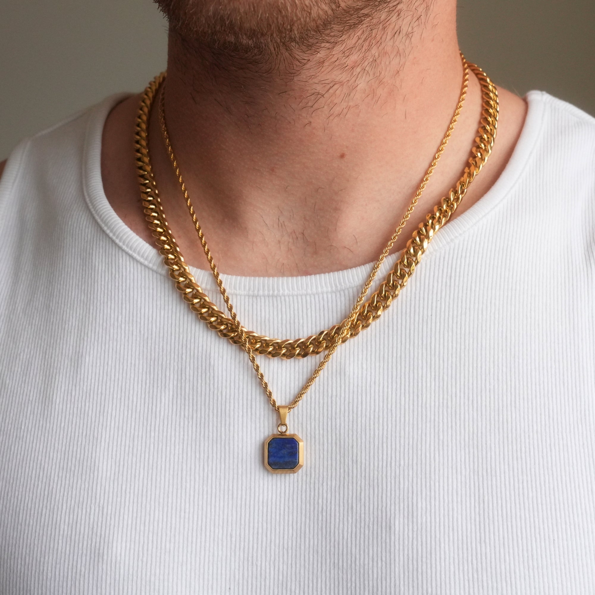 Person wearing a gold chain necklace with a blue pendant on a plain background