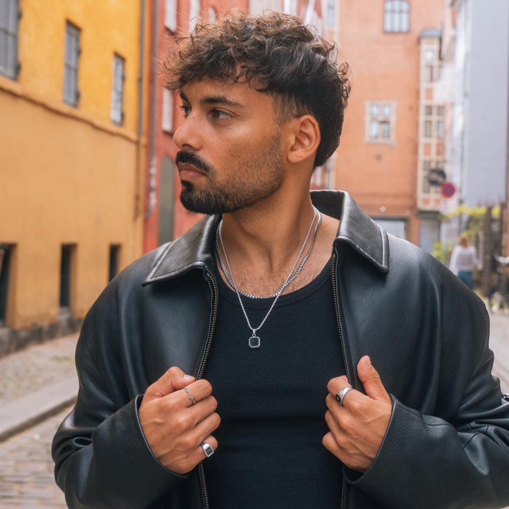 Man wearing a black leather jacket and black shirt on a street with colorful buildings.