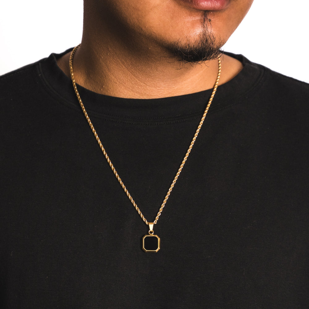 Man wearing a gold necklace with a square pendant on a black shirt