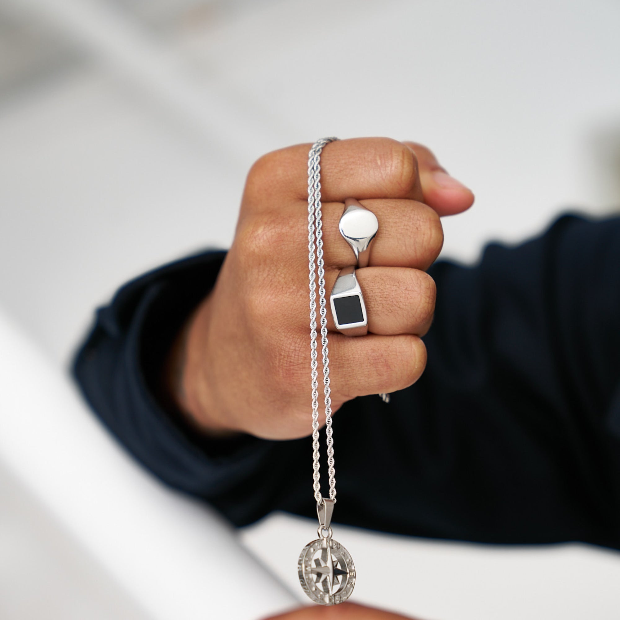 Hand wearing a silver ring and necklace with a blurred background
