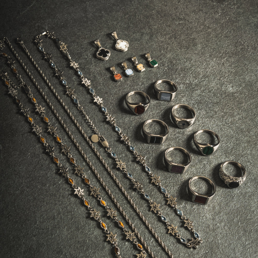 Silver jewelry including necklaces and rings on a dark surface