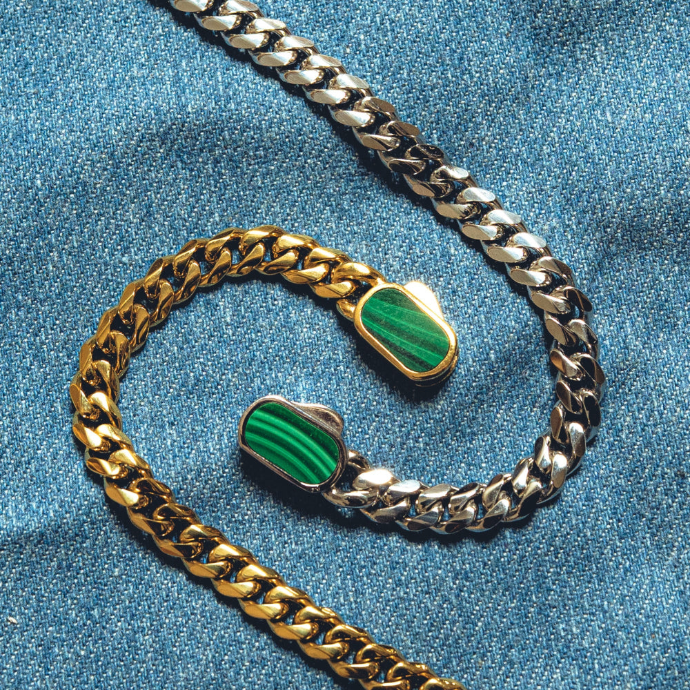 Two gold chains with green stone pendants on a blue denim background