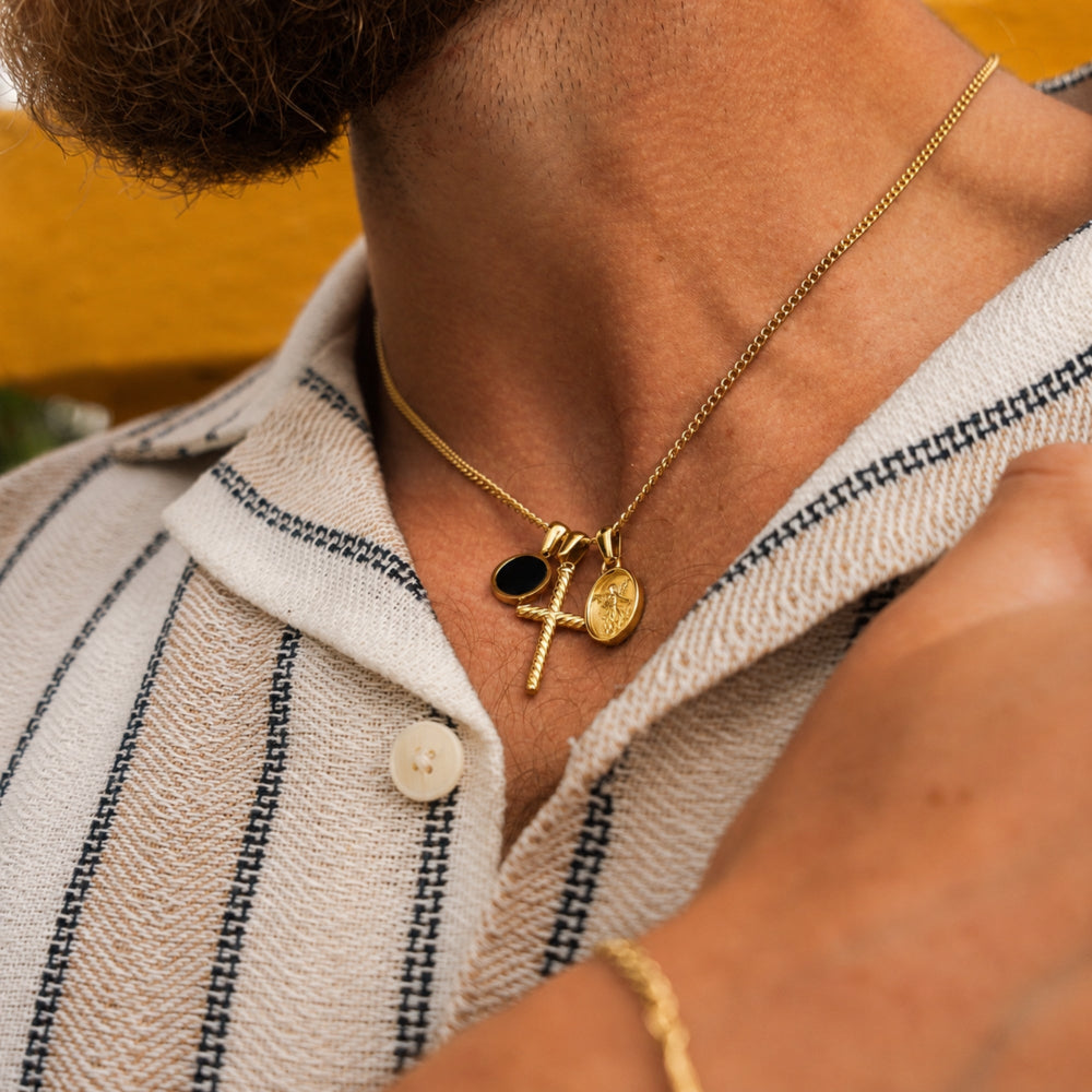 Close-up of a person wearing a gold necklace with multiple pendants, set against a blurred background.
