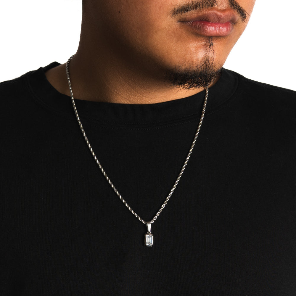 Man wearing a black shirt with a silver necklace featuring a rectangular pendant.