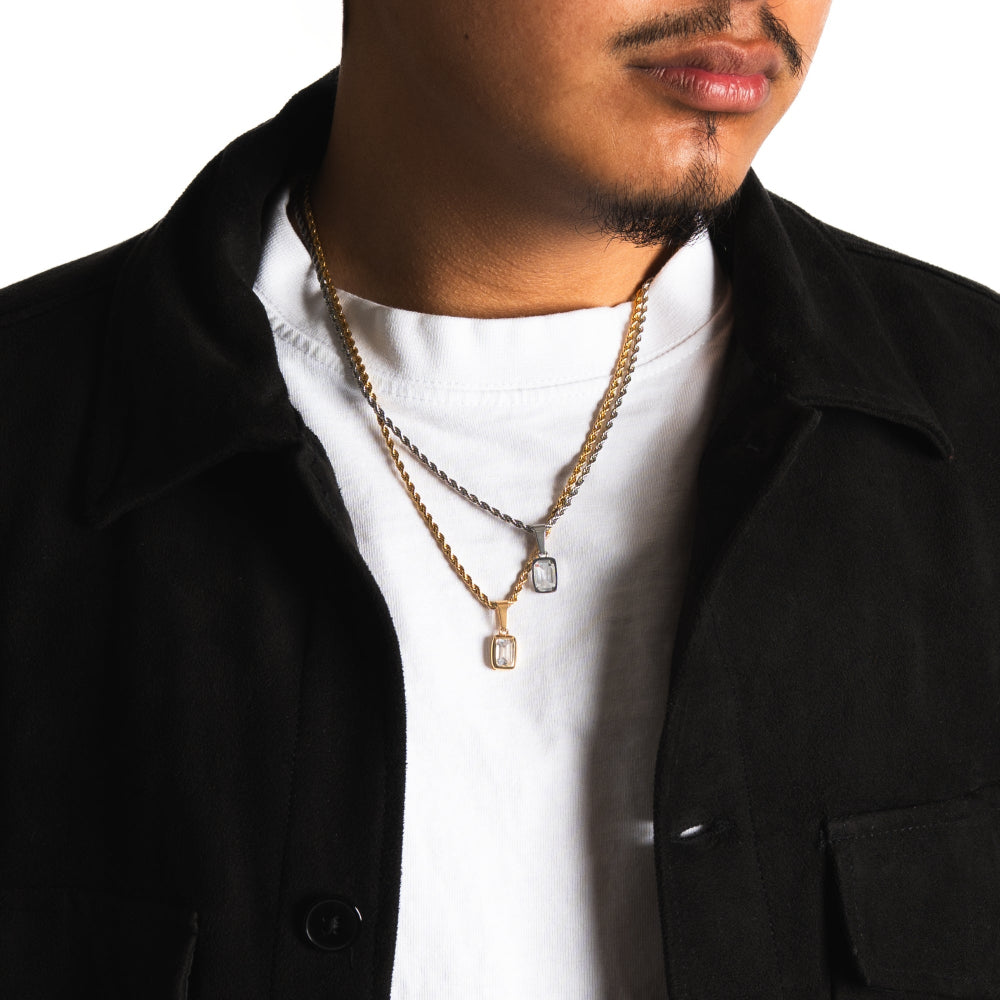 Man wearing a black jacket over a white shirt with multiple necklaces.