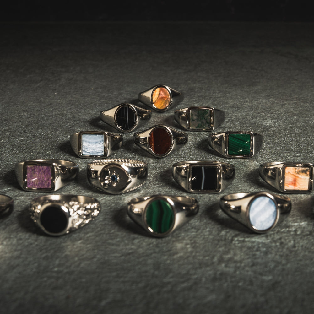 Collection of various silver rings with colored gemstones on a dark surface