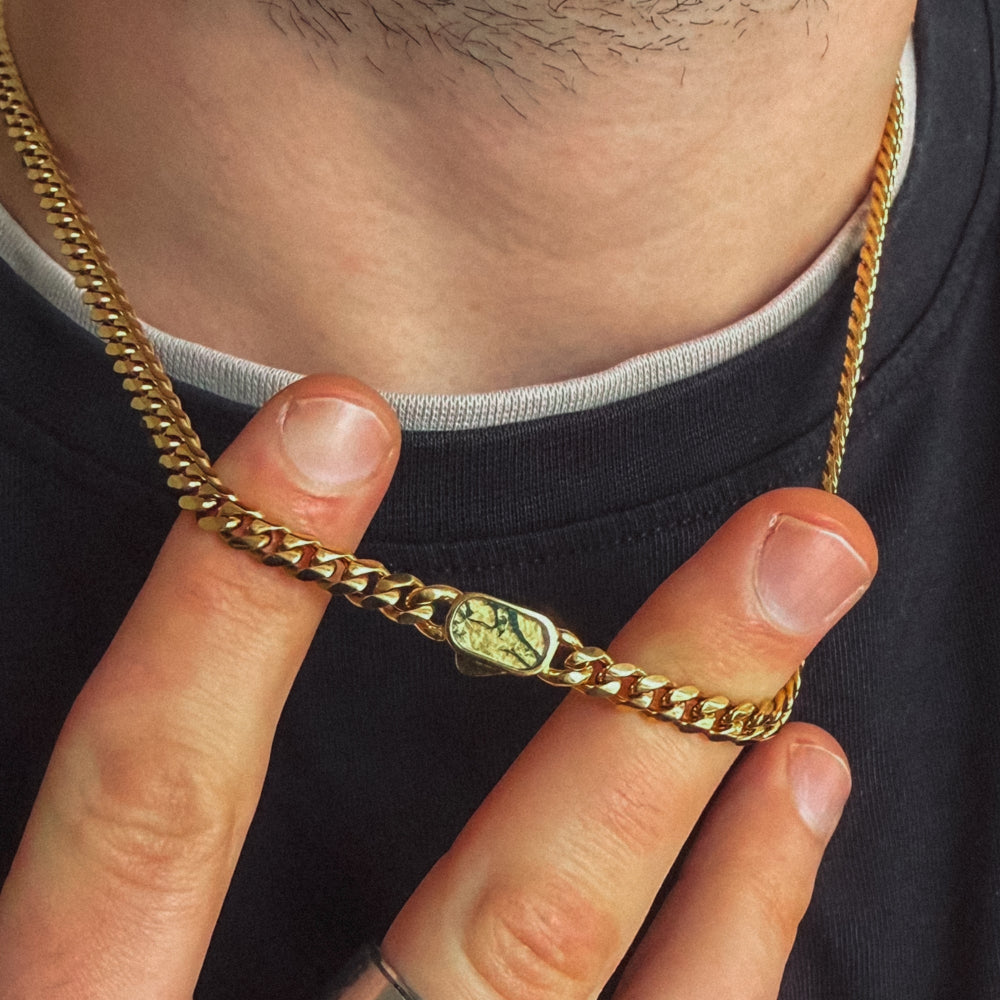 Gold chain with a green stone pendant held by a hand against a black shirt background
