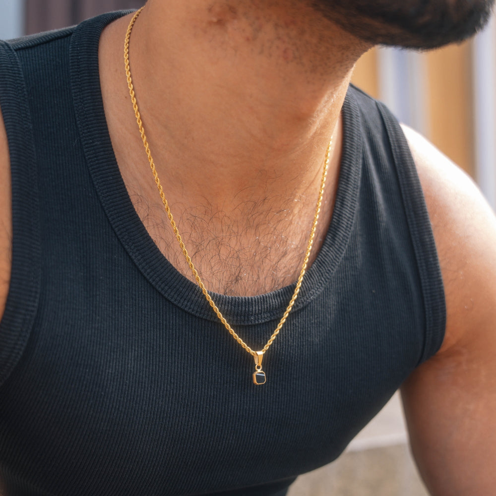 Person wearing a gold necklace with a small pendant on a black shirt.