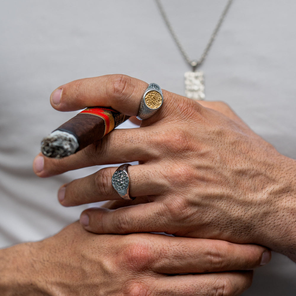 Close-up of a hand holding a cigar with rings on a neutral background