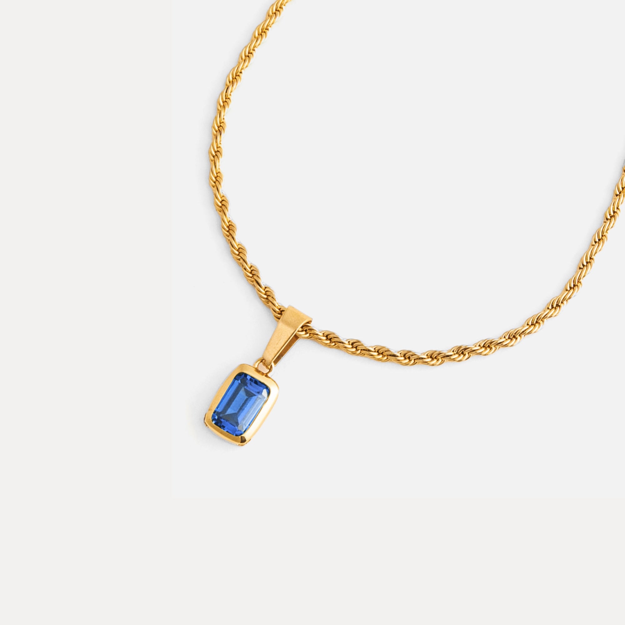 Gold necklace with a blue gemstone pendant on a white background