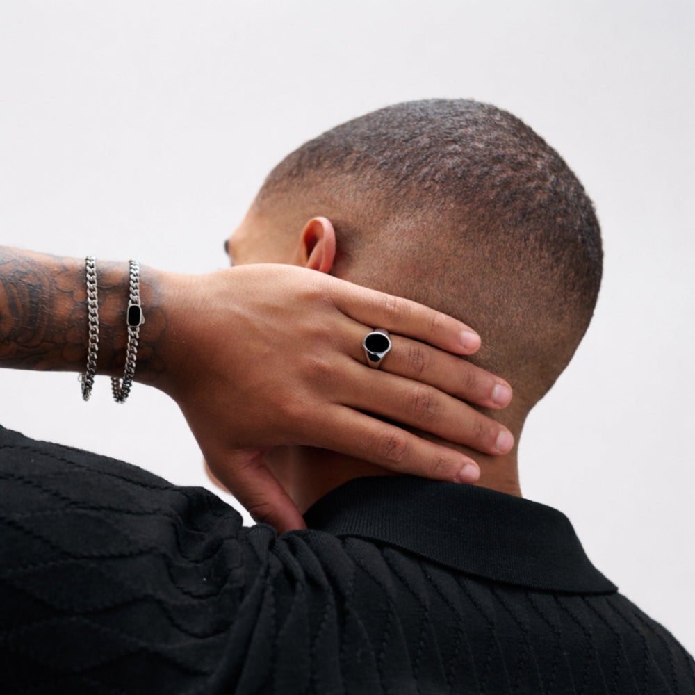 Person wearing a black shirt and silver jewelry with a neutral background