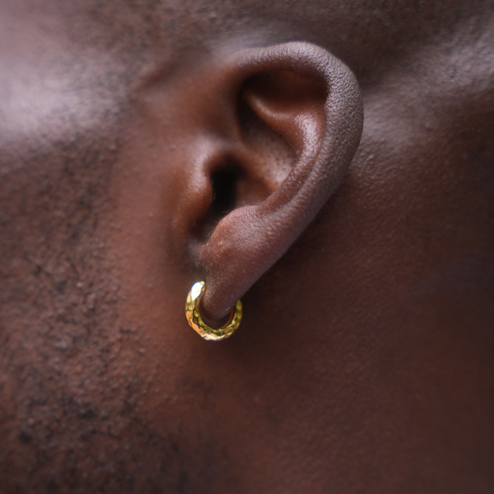 Close-up of an ear wearing a gold hoop earring on a dark background