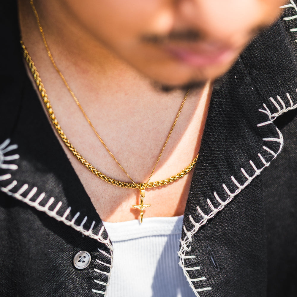 Person wearing a gold chain necklace with a cross pendant, against a blurred background.
