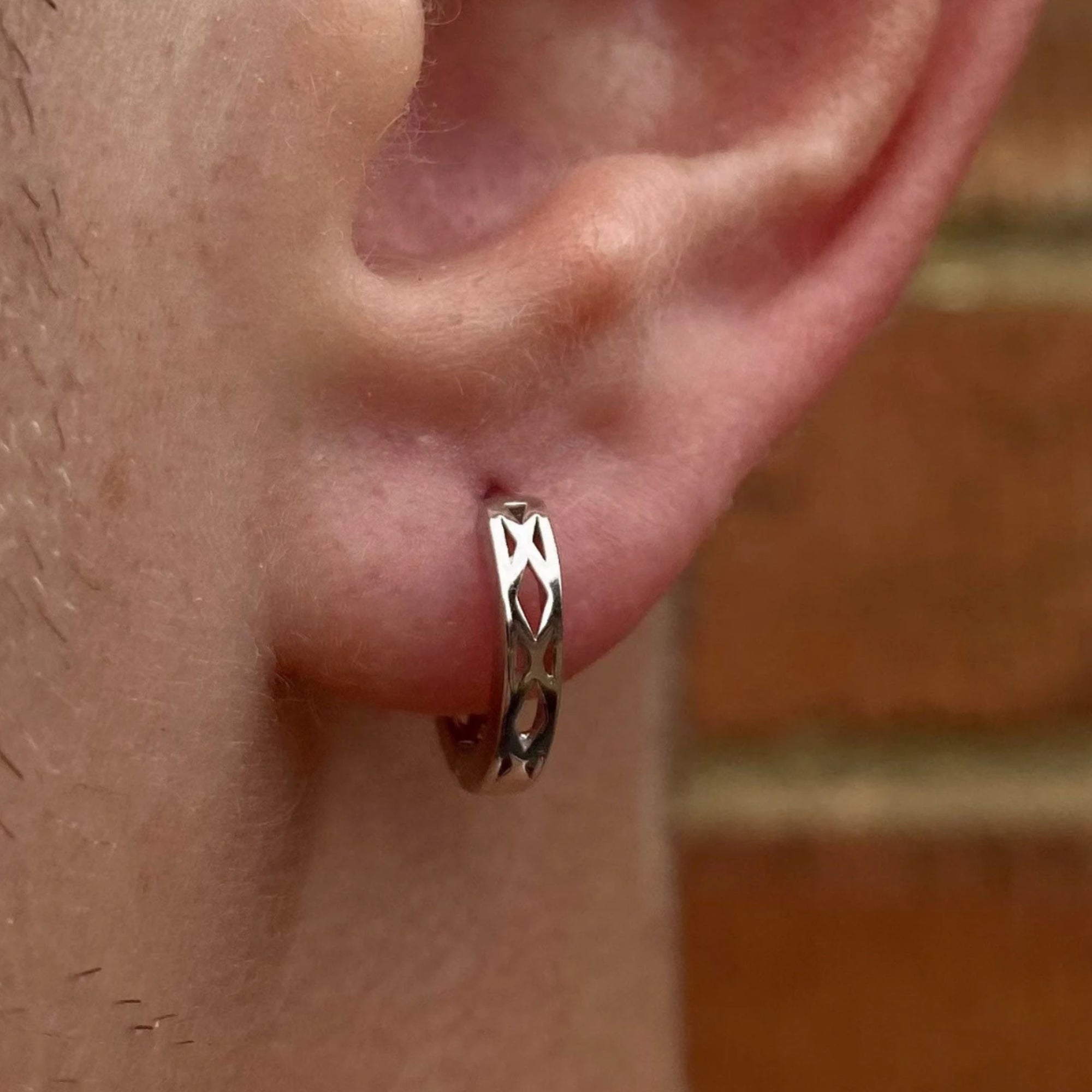 Silver hoop earring worn on an ear with a blurred background