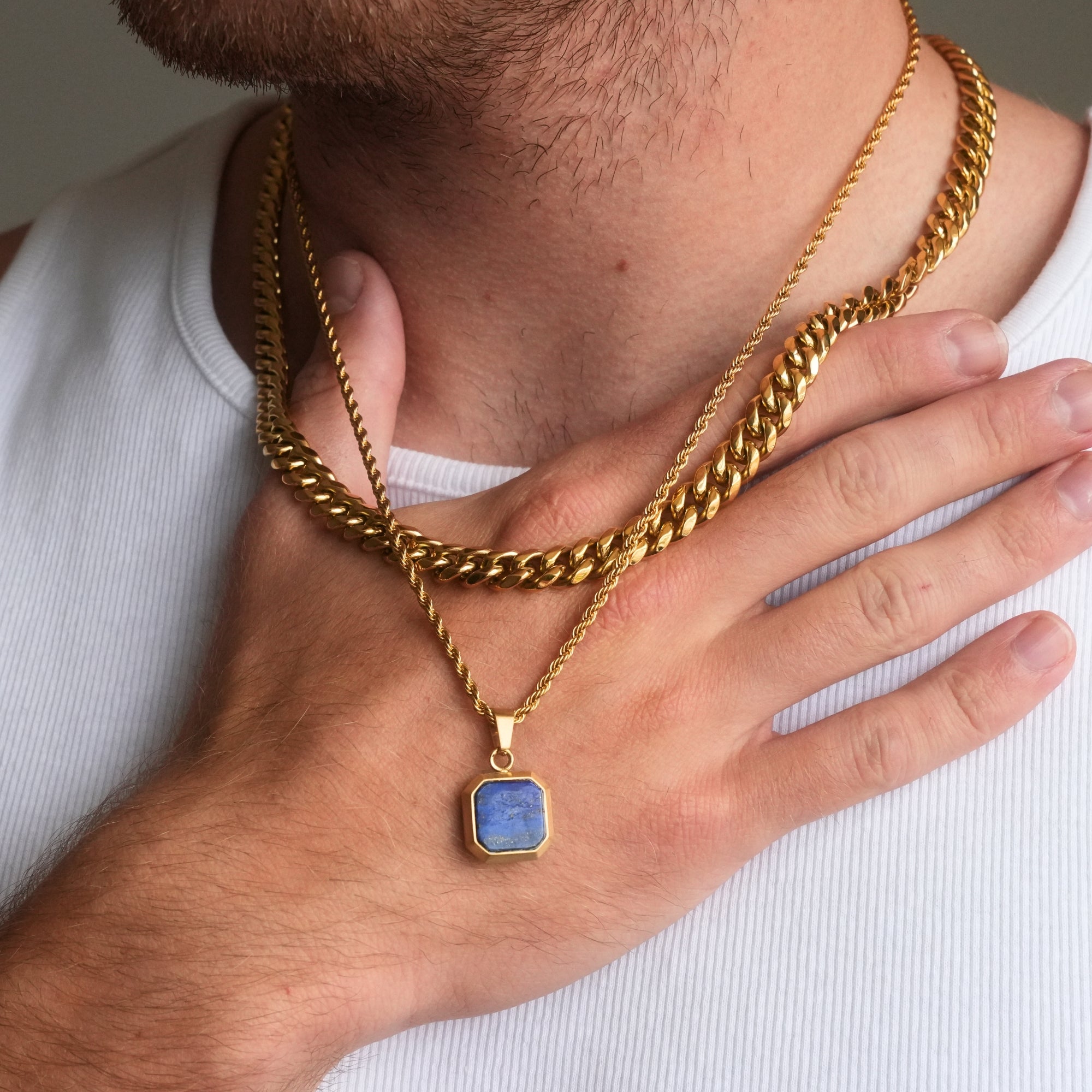 Gold chain necklace with a blue pendant worn by a person on a white background
