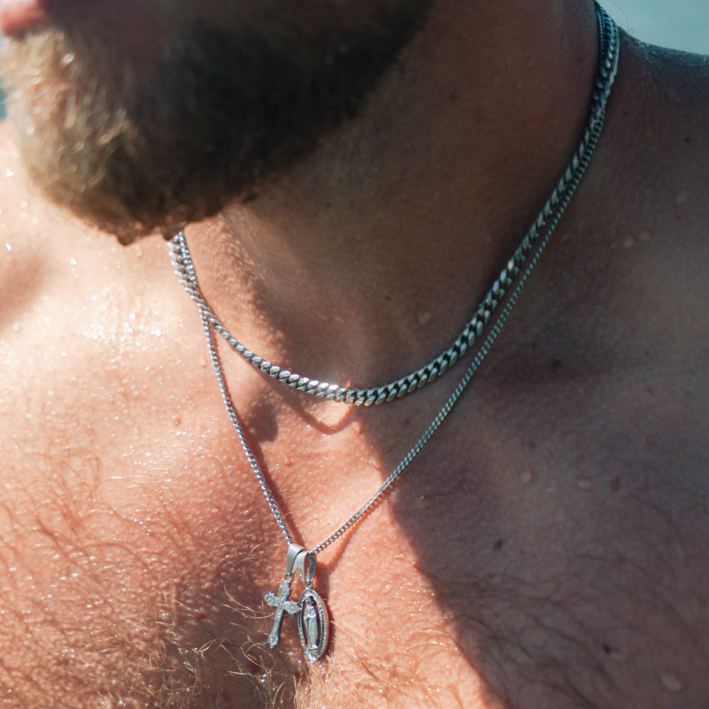 Close-up of a person wearing two silver necklaces with pendants on a sunlit background.
