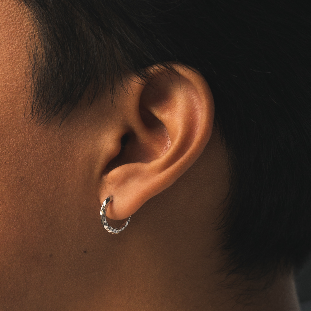 Close-up of an ear wearing a silver hoop earring with a dark background