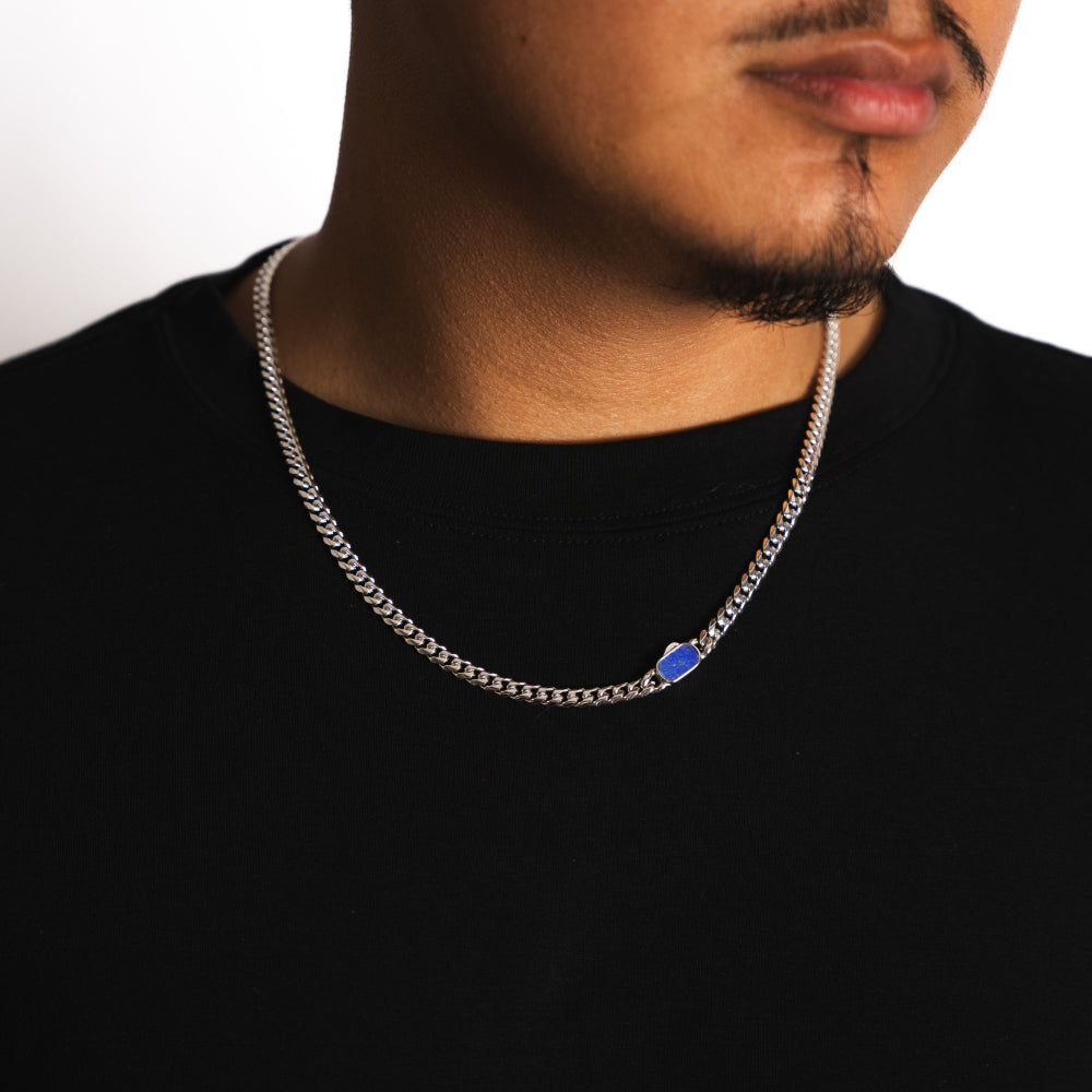 Man wearing a silver chain necklace with a blue pendant on a white background