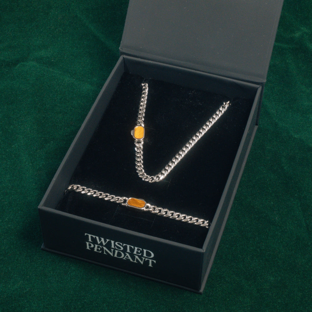 Silver chain necklace with orange pendant in a 'Twisted Pendant' box on a green background